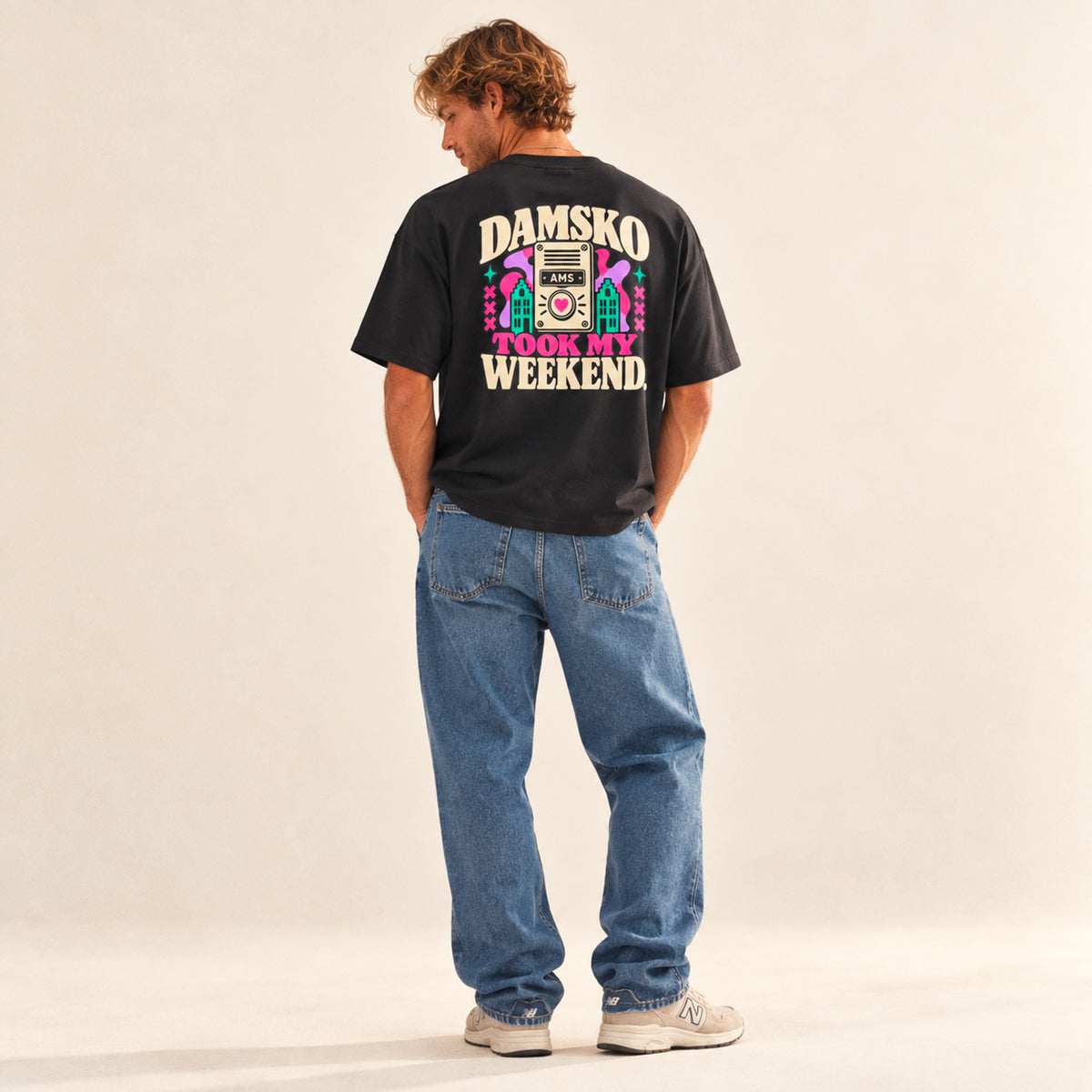 T-shirt boxy Damsko Beauséjour vu de dos, avec imprimé multicolore « Damsko Took My Weekend », interphone AMS et façades d’Amsterdam.