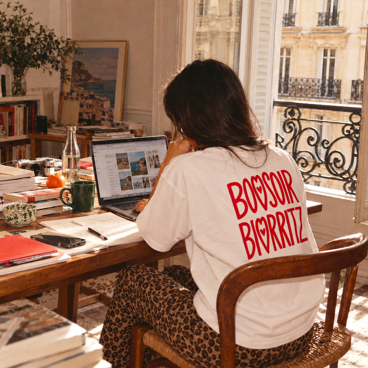 T-shirt blanc Beauséjour Bonsoir Biarritz avec grand imprimé rouge au dos, porté par une femme dans un intérieur lumineux, style lifestyle inspiré de Biarritz.