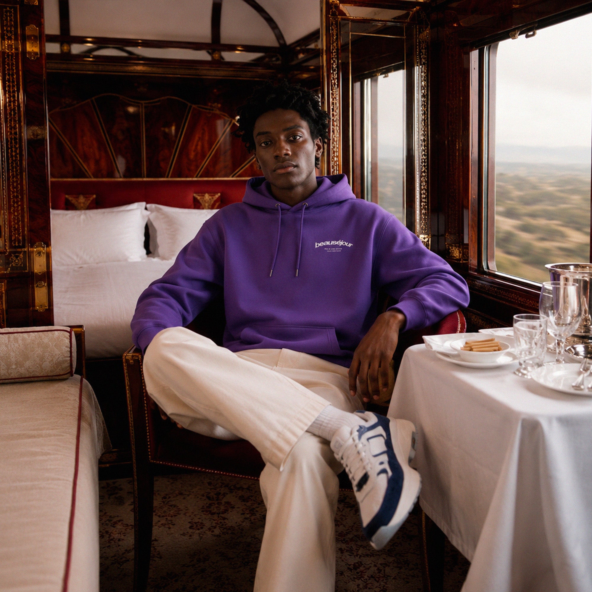 Hoodie Room 27 Venice Beauséjour Orient Express, coloris violet profond, logo poitrine minimaliste et grand imprimé dos "Beauséjour — Meet Me After Midnight — Room 27 Venice Stopover", capuche ajustable et poche kangourou, look complet.