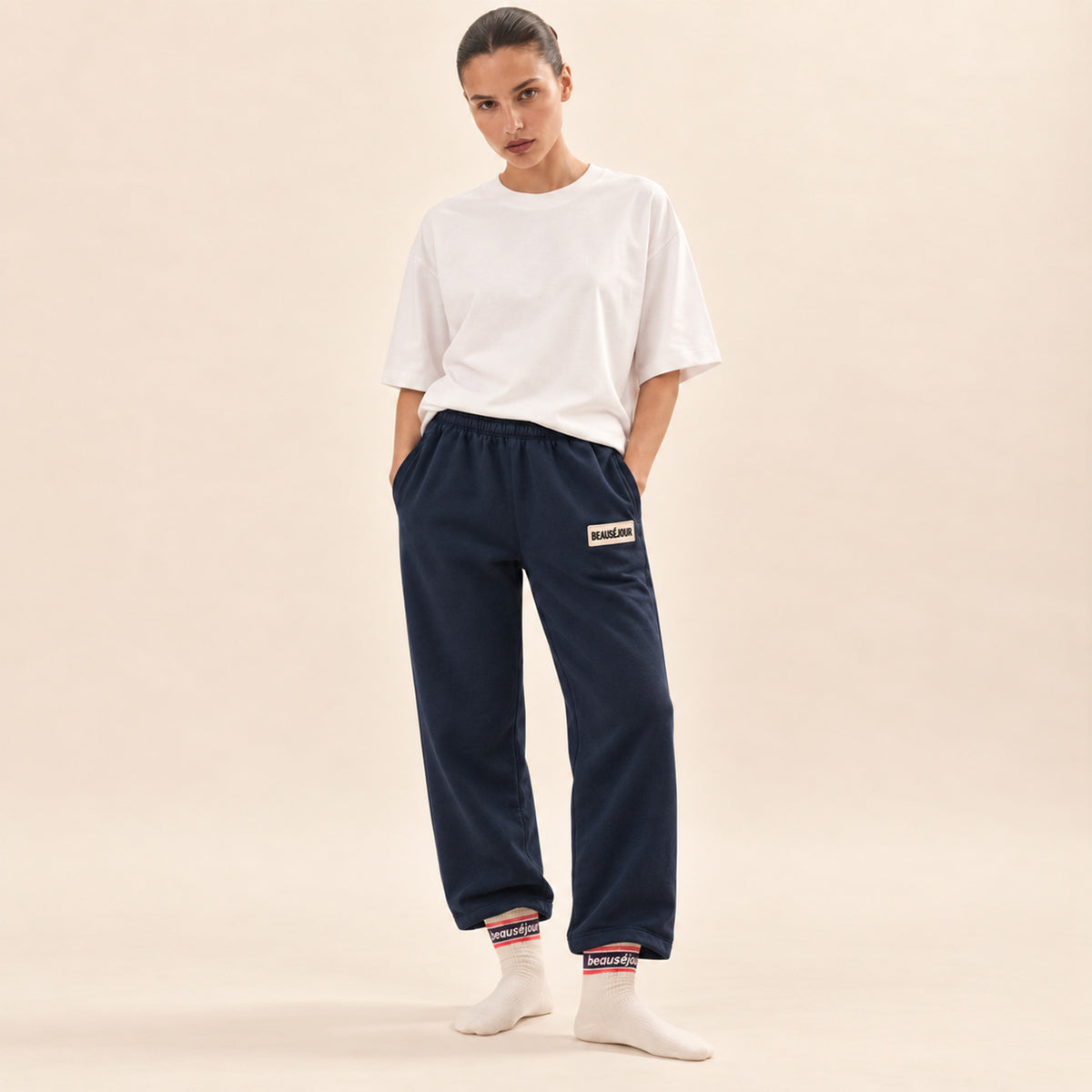 Jogging bleu marine femme Beauséjour, coupe droite et ample, taille élastique, poches latérales et patch brodé écru avec logo noir sur la cuisse.