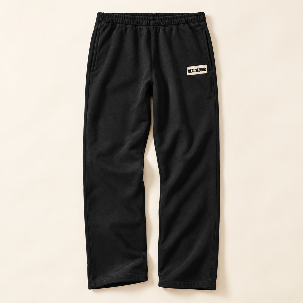 Jogging noir femme Beauséjour, coupe droite et ample, taille élastique, poches latérales et patch brodé écru avec logo noir sur la cuisse.