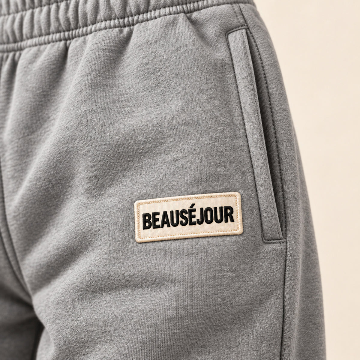 Jogging gris femme Beauséjour, coupe droite et ample, taille élastique, poches latérales et patch brodé écru avec logo noir sur la cuisse. zoom produit.
