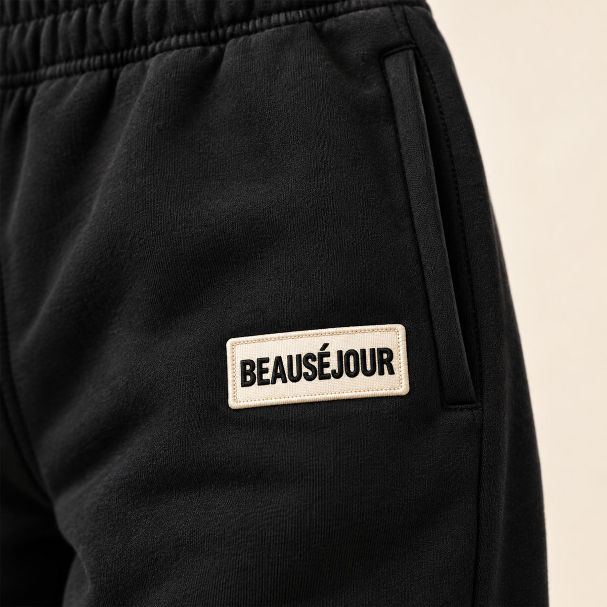 Jogging noir femme Beauséjour, coupe droite et ample, taille élastique, poches latérales et patch brodé écru avec logo noir sur la cuisse. Zoom produit.