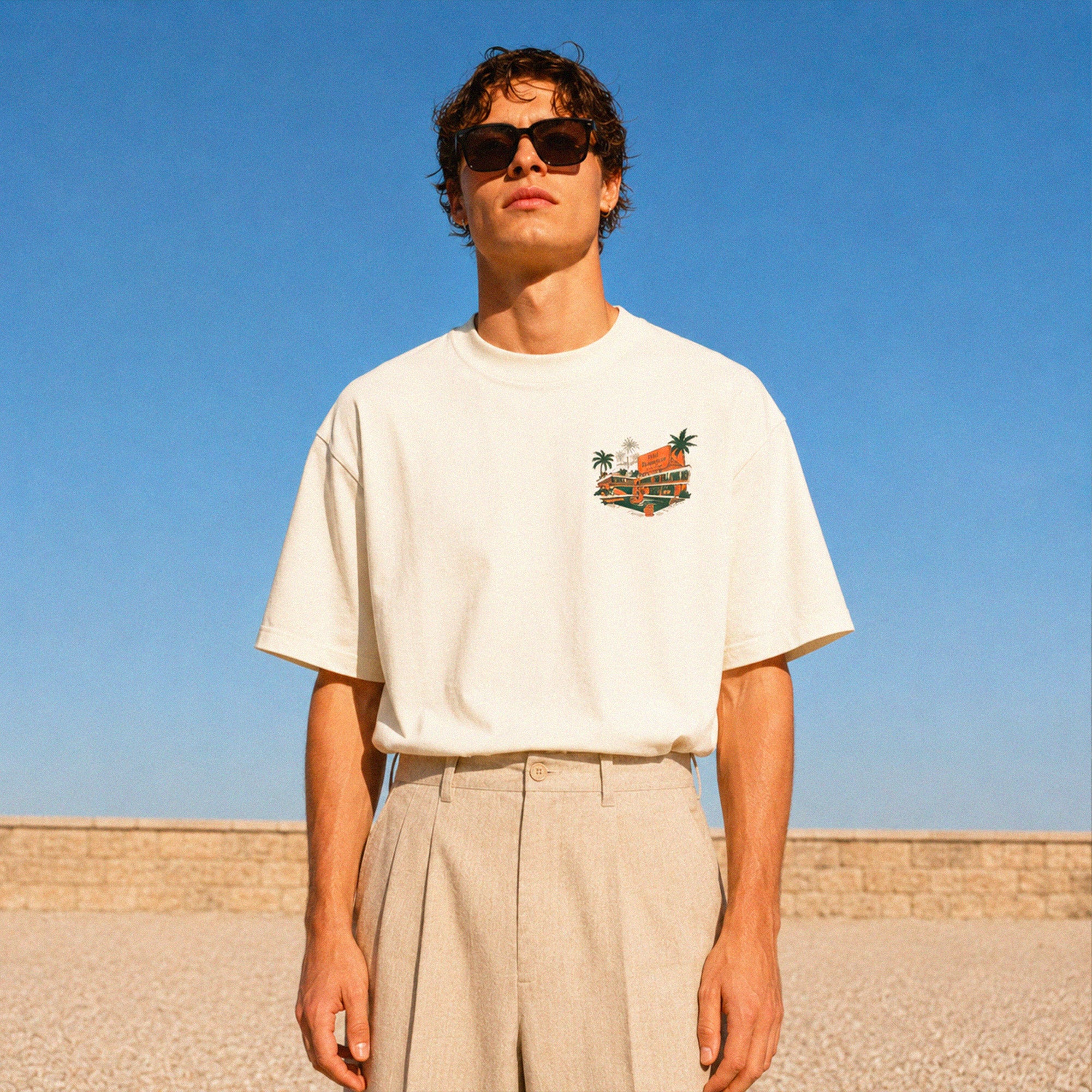 T-shirt boxy Hôtel Beauséjour 200 GSM porté avec pantalon beige, style élégant et décontracté pour les beaux jours.