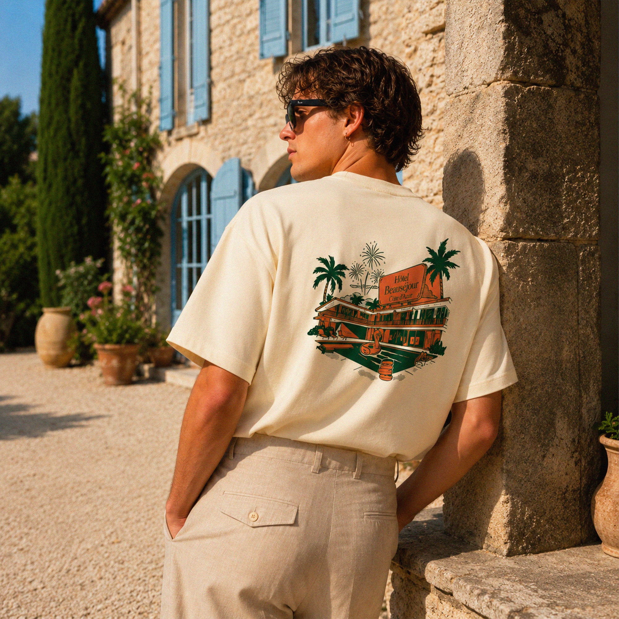 T-shirt boxy crème Hôtel Beauséjour avec grand imprimé dos vintage représentant un hôtel Riviera avec palmiers et ambiance vacances d’été.