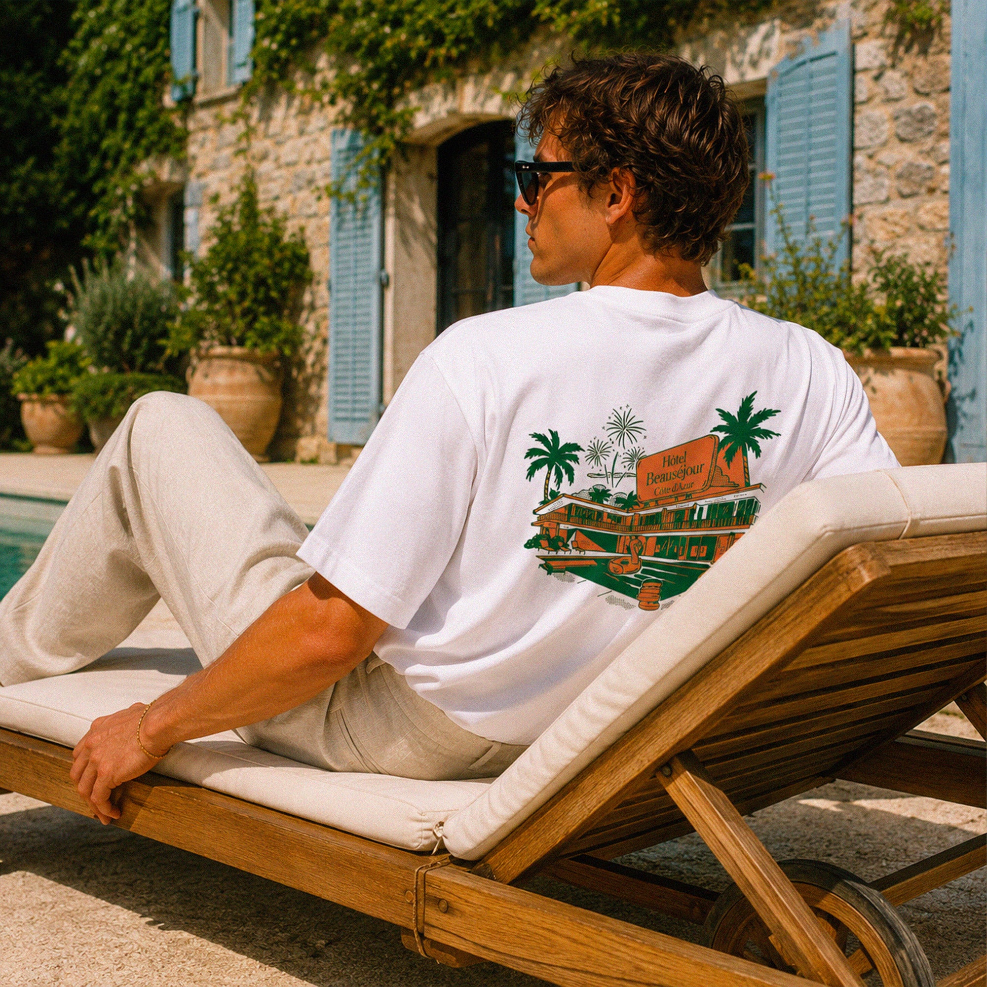 Homme portant le t-shirt Hôtel Beauséjour coupe oversize 200 grammes au bord d’une piscine méditerranéenne.