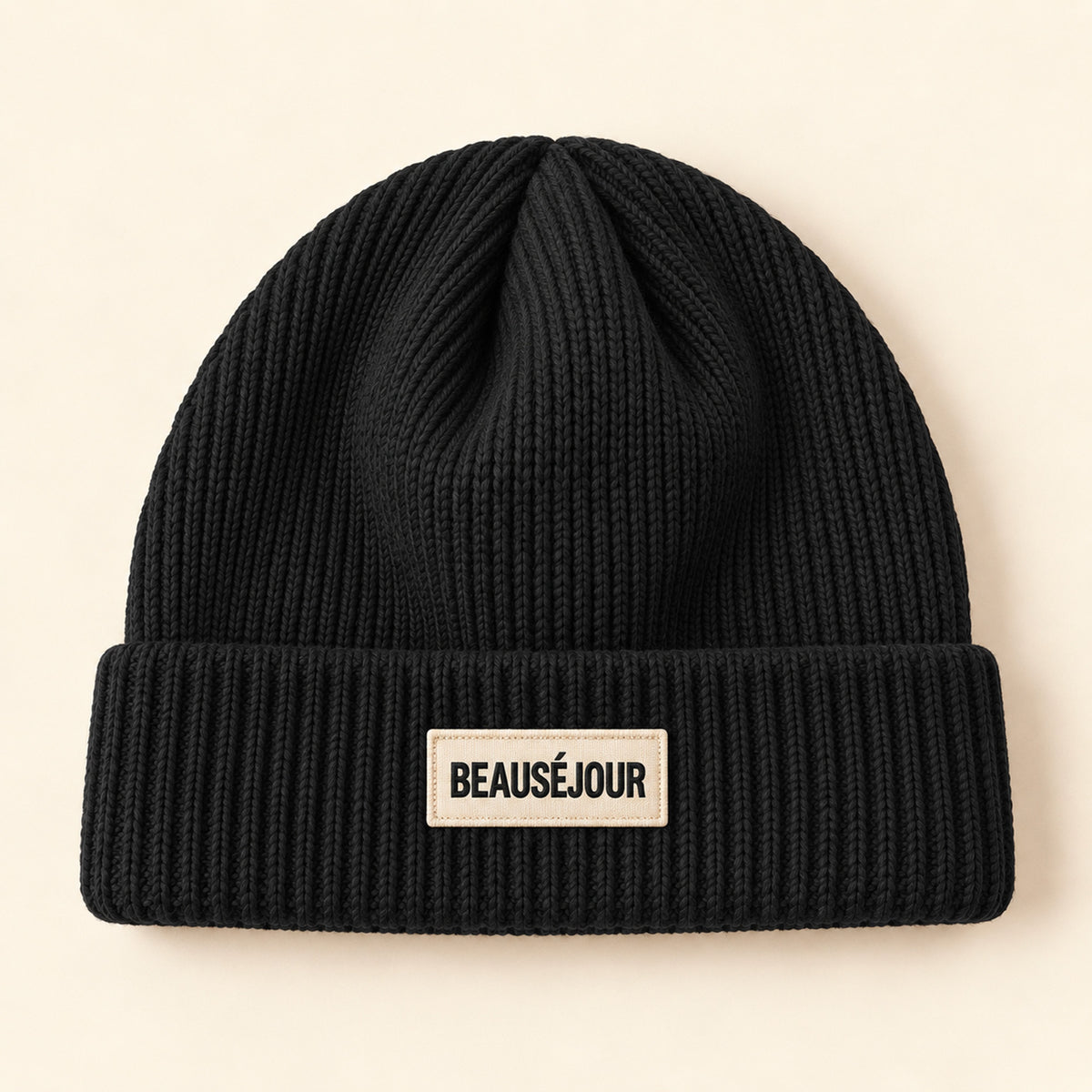 Bonnet noir Beauséjour en coton biologique, maille côtelée avec double revers et patch brodé écru à logo noir sur le devant.