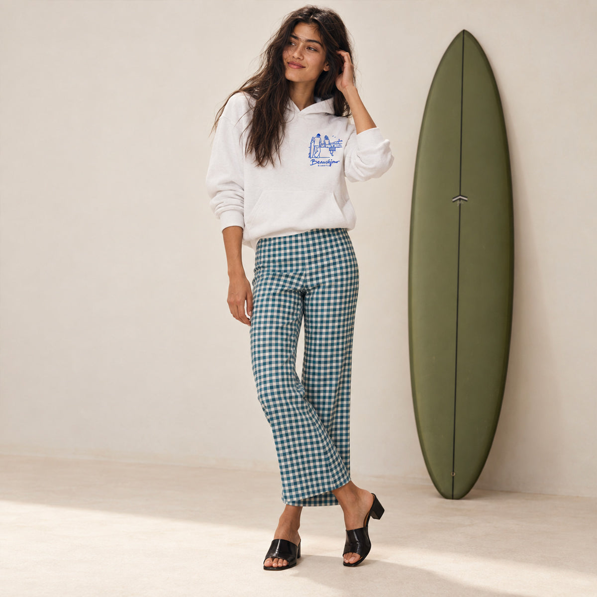 Hoodie Biarritz after surf blanc porté par une femme debout à côté d'une planche de surf verte, vue de face