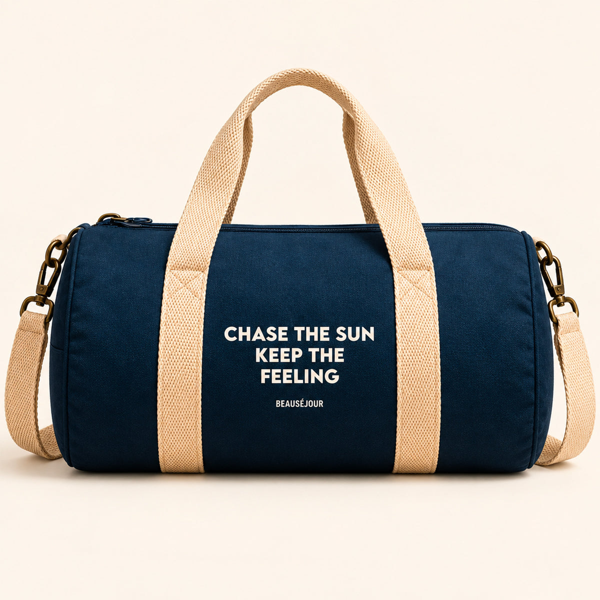 Sac de sport Beauséjour bleu marine, format polochon, avec anses et bandoulière écrues, fermeture zippée et inscription blanche « Chase the Sun, Keep the Feeling ».
