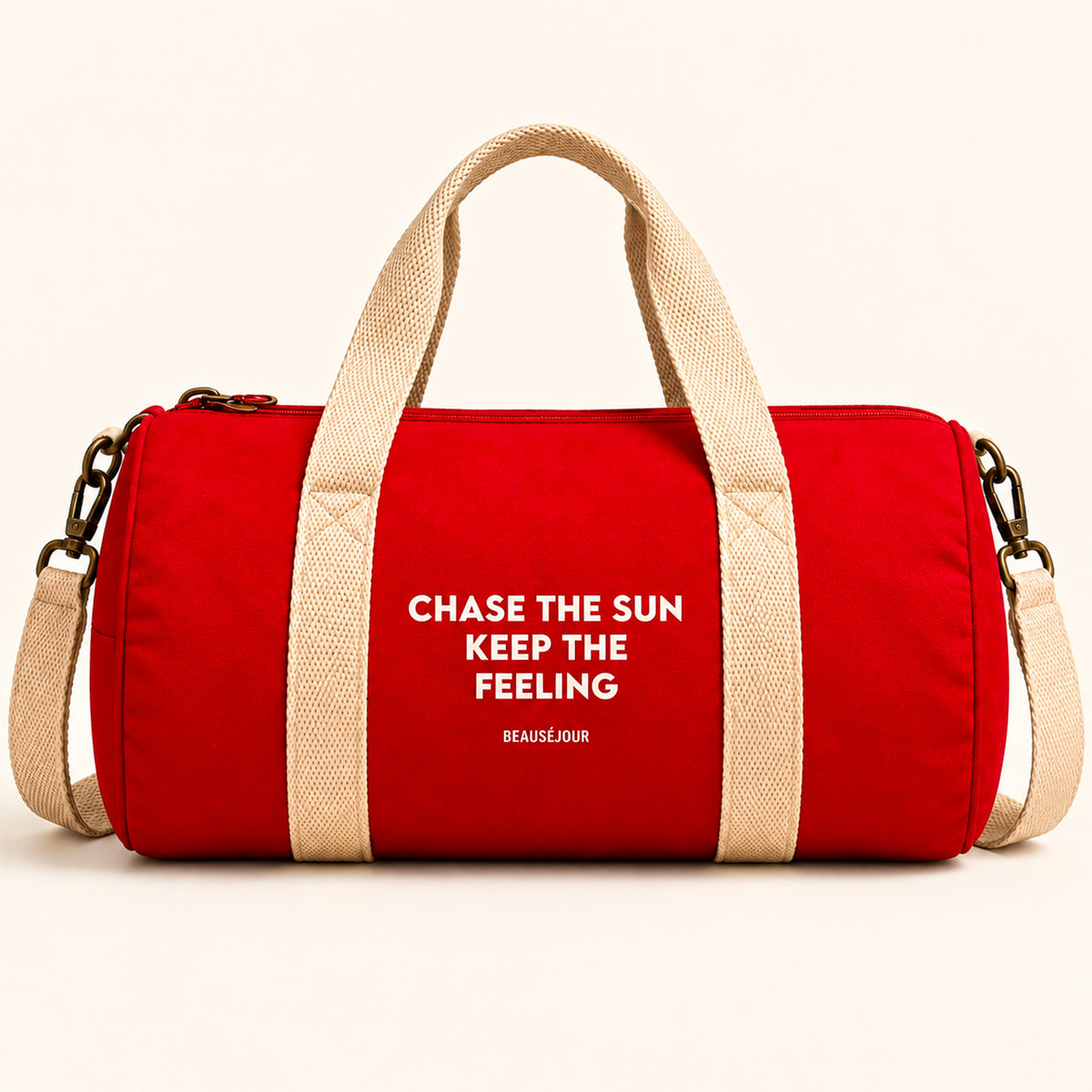 Sac de sport Beauséjour rouge, format polochon, avec anses et bandoulière écrues, fermeture zippée et inscription blanche « Chase the Sun, Keep the Feeling ».
