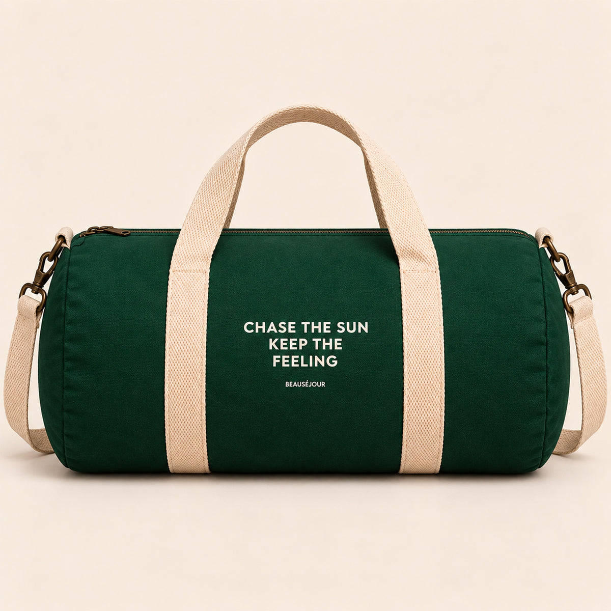 Sac de sport Beauséjour vert foncé, format polochon, avec anses et bandoulière écrues, fermeture zippée et inscription blanche « Chase the Sun, Keep the Feeling ».