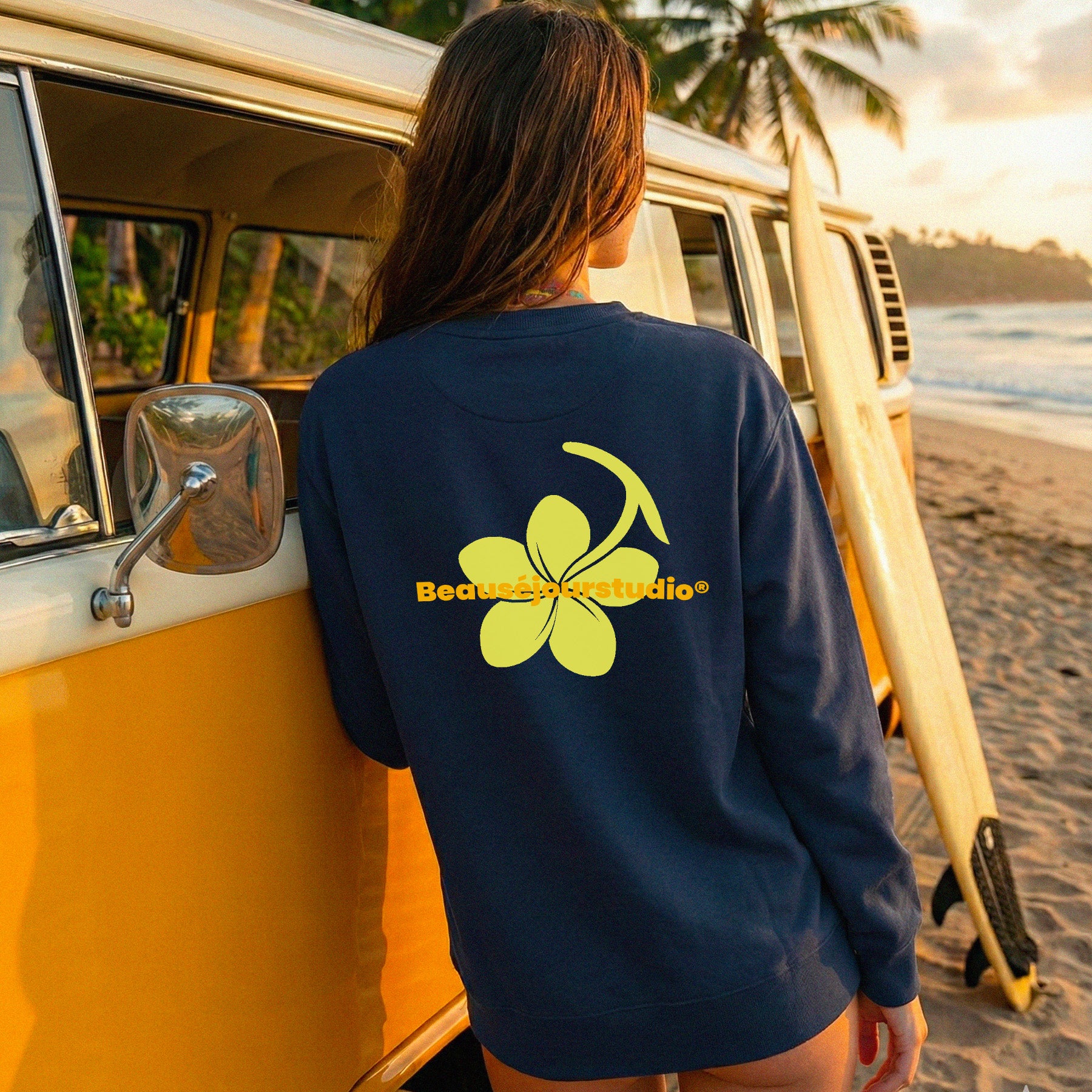Femme sur une plage à Bali. Elle porte un sweatshirt bleu marine col rond. Fleur Plumeria jaune imprimée au dos du sweat. Le sweatshirt parfait pour le yoga.