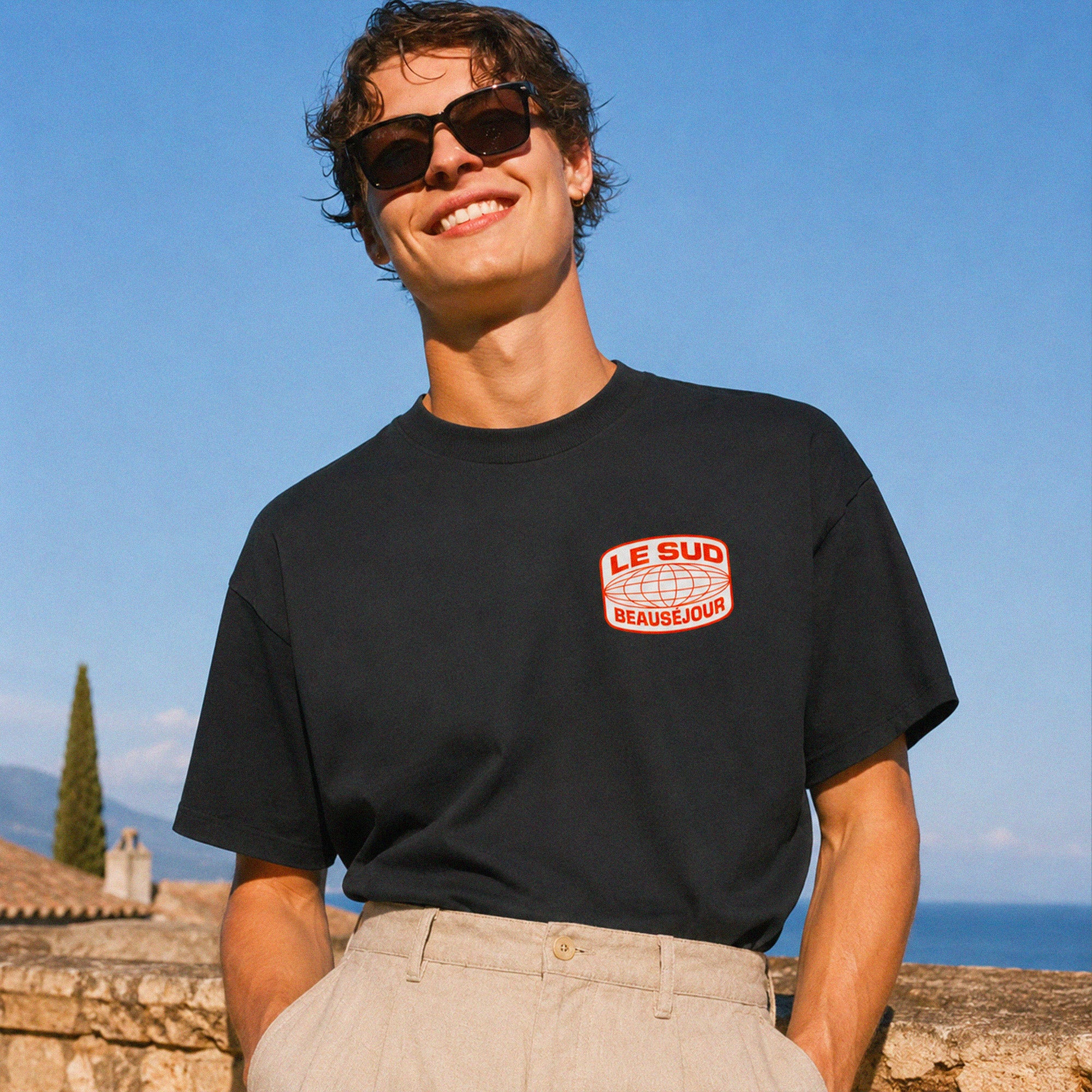 T-shirt oversize noir Beauséjour Le Sud en coton 200 grammes porté avec pantalon beige, coupe boxy et inspiration Côte d’Azur.