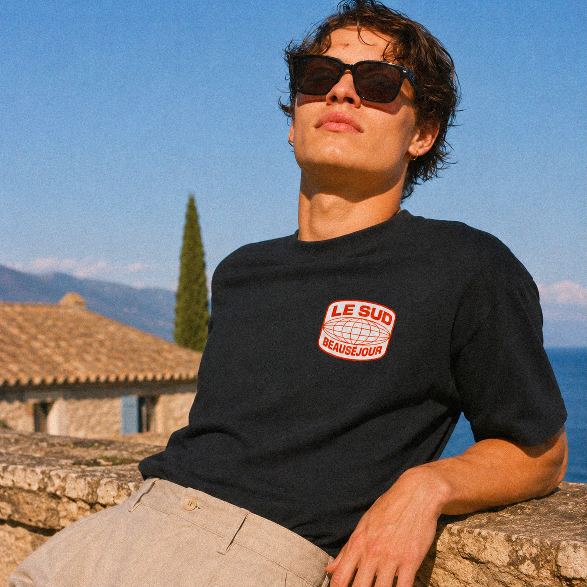 face du t-shirt boxy noir Beauséjour avec imprimé Le Sud, porté devant une maison provençale pendant l’été.