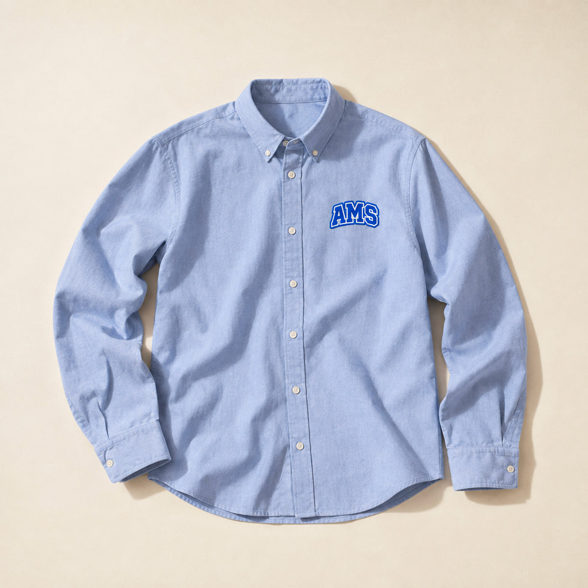 Chemise Oxford homme Beauséjour AMS bleu ciel en coton biologique, coupe élégante avec col classique, boutons blancs et patch AMS brodé sur la poitrine.