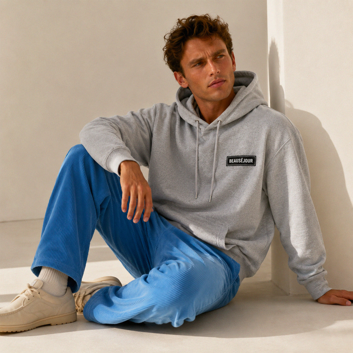 Hoodie basique Beauséjour® coloris gris, détail du patch Beauséjour noir sur blanc en poitrine et de la capuche.