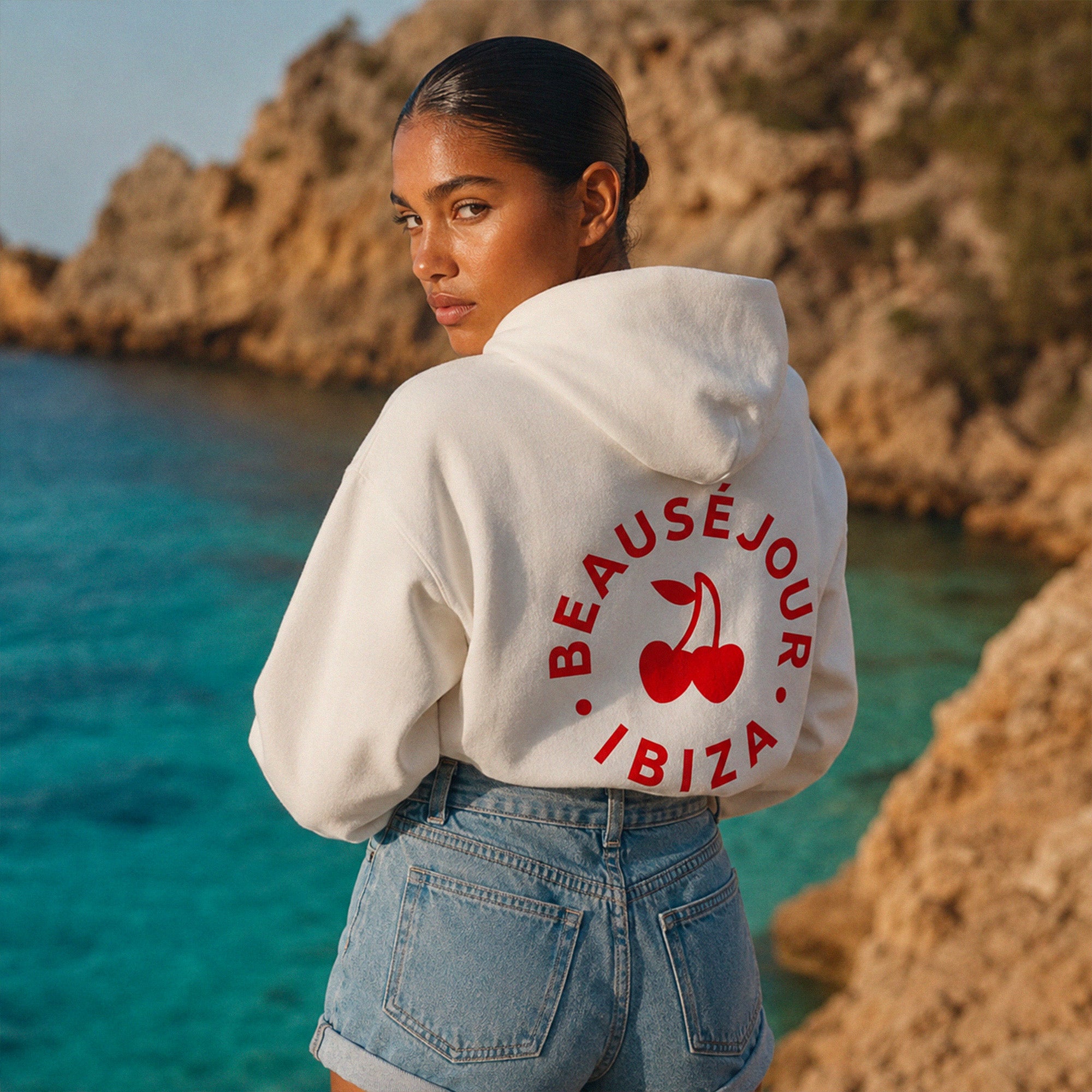 Hoodie blanc oversize Beausejour Ibiza avec imprime rouge et cerises sur plage rocheuse