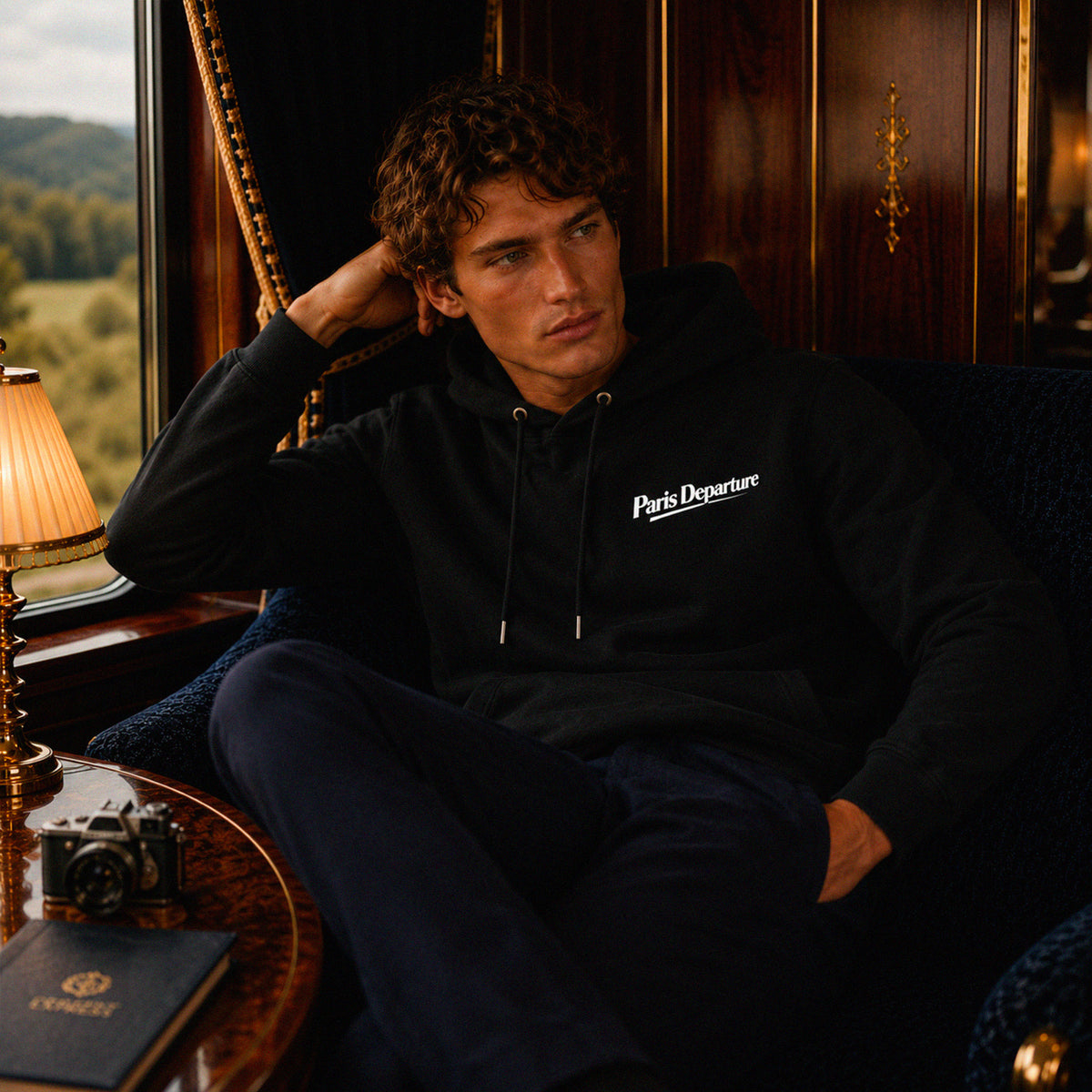 Hoodie Paris Departure Beauséjour Orient Express, coloris noir profond, 100% coton biologique molleton brossé, imprimé Paris Departure côté cœur et marquage dos inspiré des compagnies de voyage anciennes, détail de la capuche et du col.