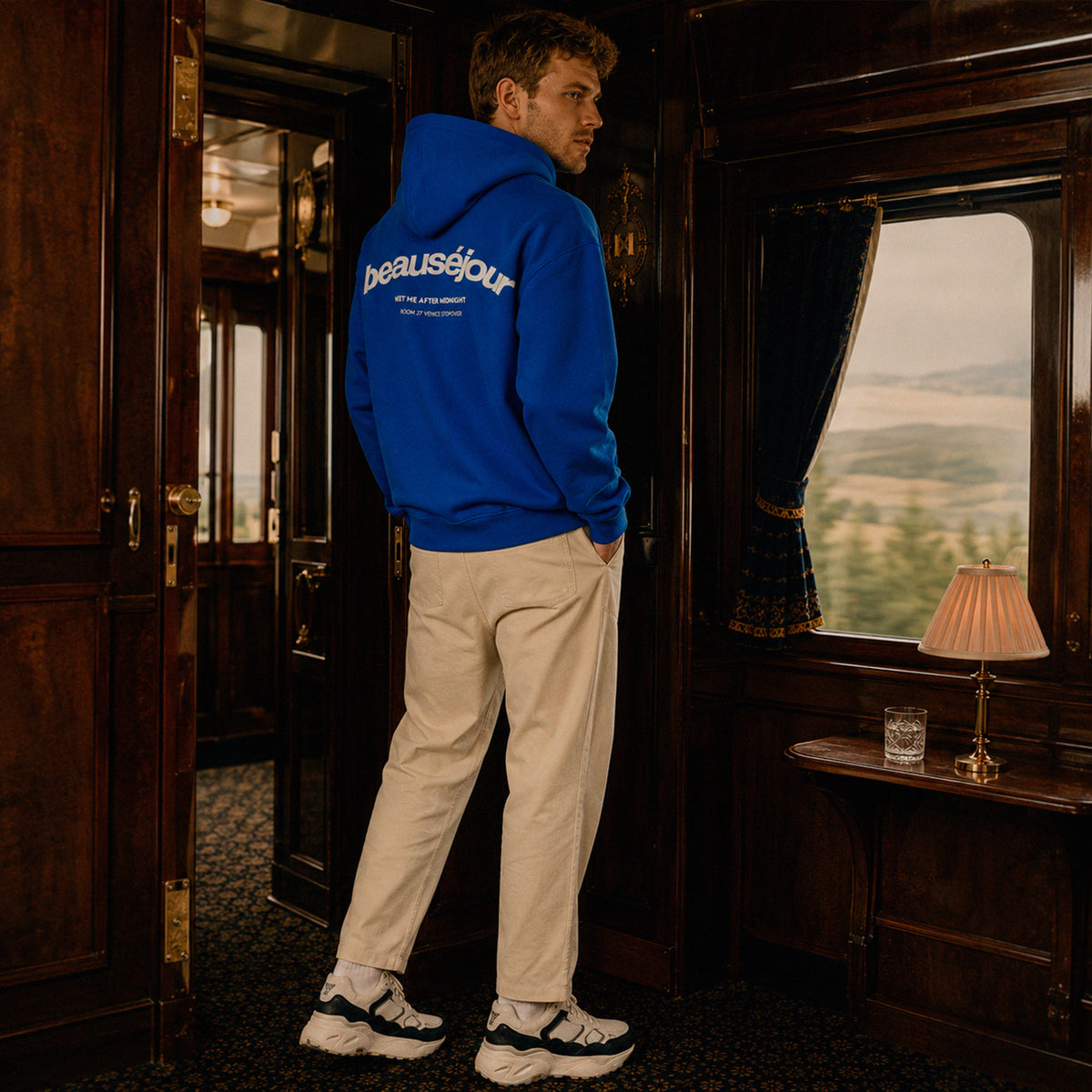 Hoodie Room 27 Venice Beauséjour Orient Express, coloris bleu royal, logo poitrine minimaliste et grand imprimé dos "Beauséjour — Meet Me After Midnight — Room 27 Venice Stopover", capuche ajustable et poche kangourou, vue de face.