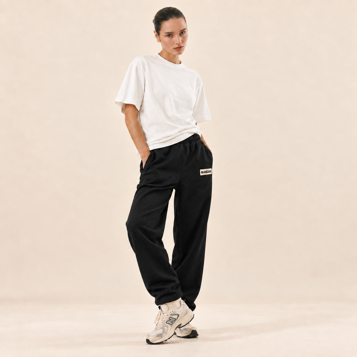 Jogging noir femme Beauséjour, coupe droite et ample, taille élastique, poches latérales et patch brodé écru avec logo noir sur la cuisse.