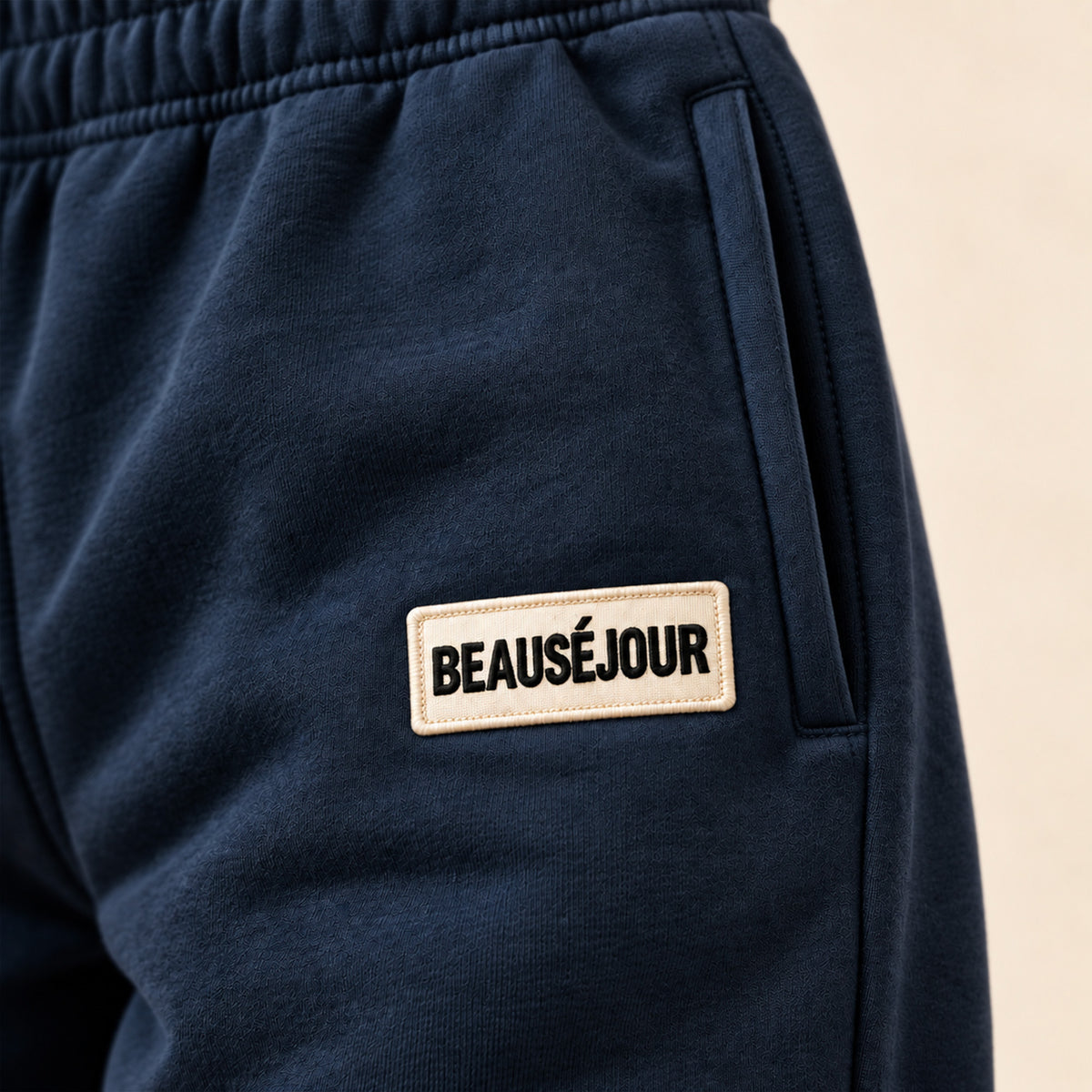 Jogging bleu marine femme Beauséjour, coupe droite et ample, taille élastique, poches latérales et patch brodé écru avec logo noir sur la cuisse. zoom produit.