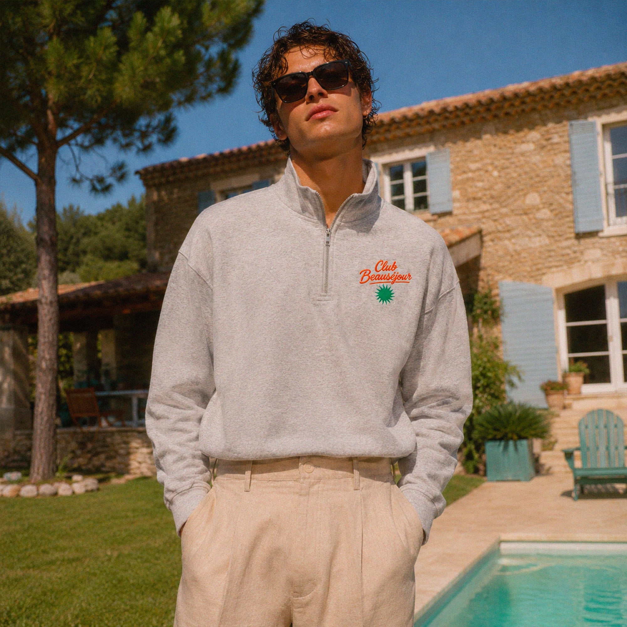 Sweat zippé gris chiné Club Beauséjour avec broderie poitrine porté au bord d’une piscine dans une maison du Sud.
