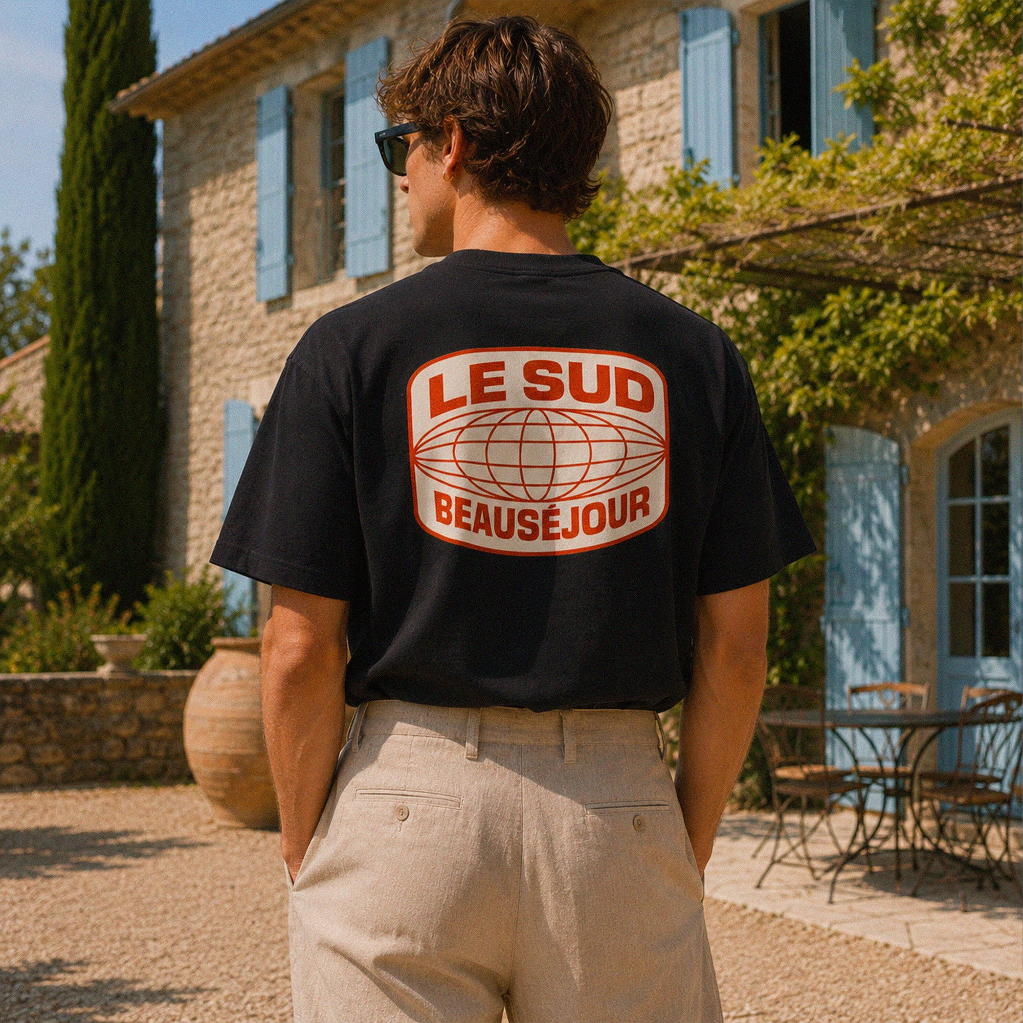 Vue arrière du t-shirt noir Le Sud Beauséjour avec grand imprimé graphique rouge et crème dans un style rétro vacances.