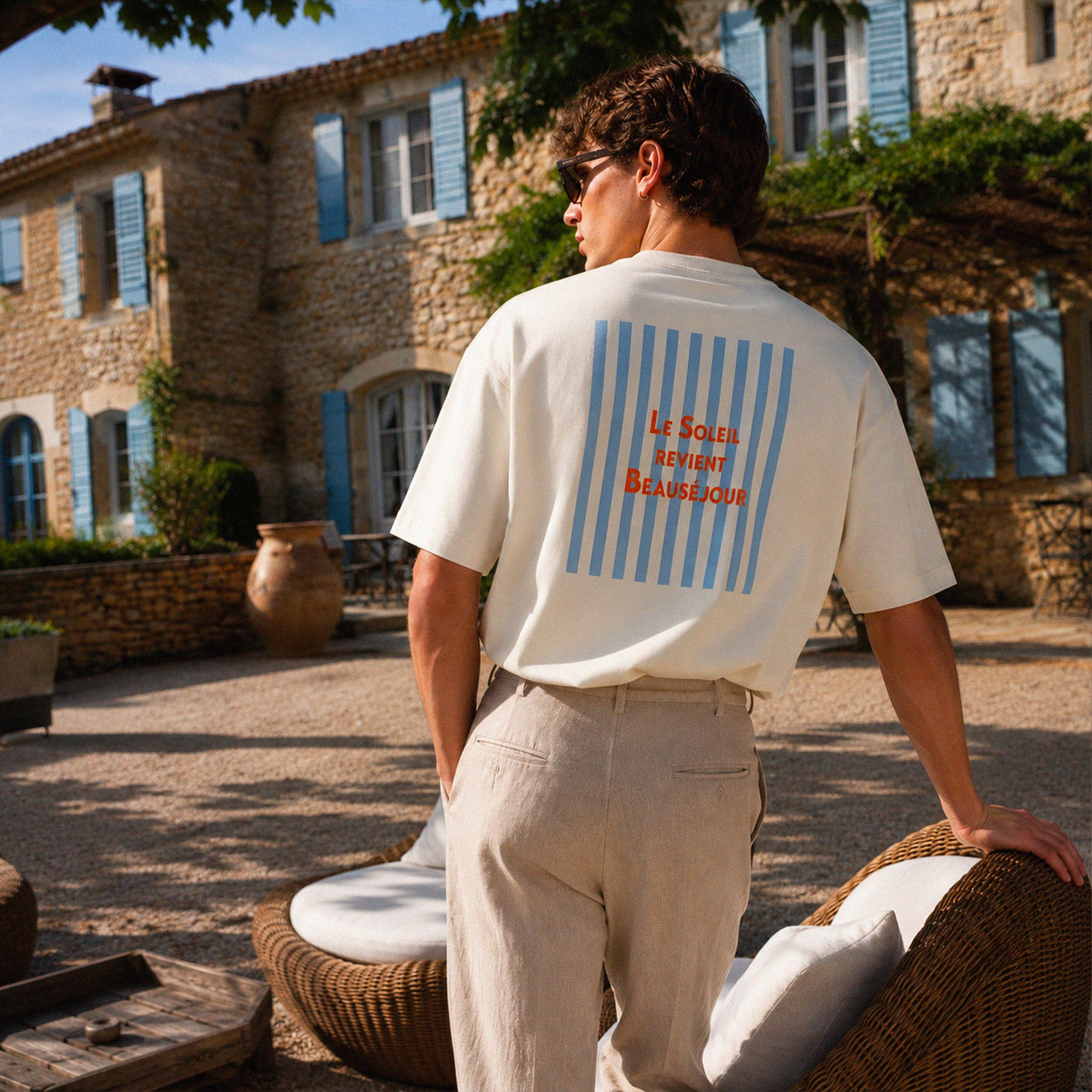 T-shirt boxy crème Le Soleil Revient Beauséjour avec grand imprimé dos bleu et rouge, porté dans une maison d’été inspiration Provence.